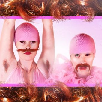 A photo of "The Merkin Sisters" rests on curly red hair. They wear pink bathing caps and moustaches.