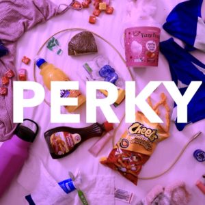 Various items rest on a pink blanket, such as a water bottle, orange juice, cheetos, a swimsuit, medication and ice cream. Above these items in a thick white font reads "Perky"