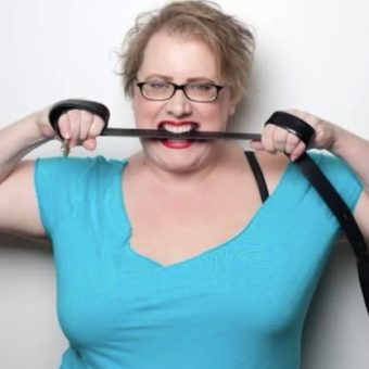 Cameryn Moore stands in front of white background chewing on black rope.